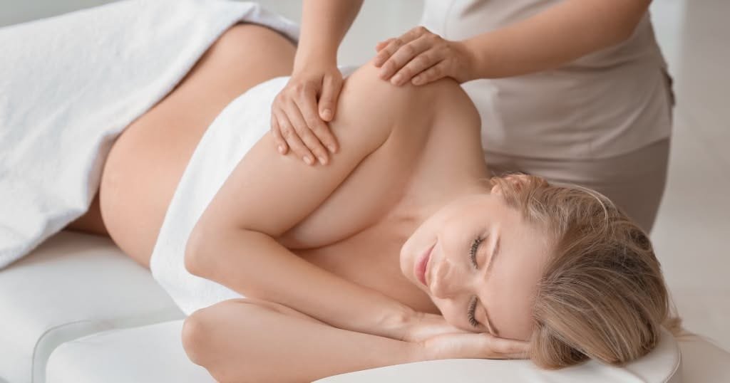 Pregnant woman resting on her side while receiving a shoulder massage.